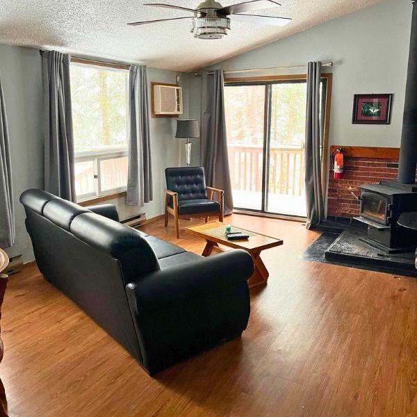 Inside one of the Chalets' living areas, showing a couch, chair, wood burning fireplace, windows, and sliding door to the deck.