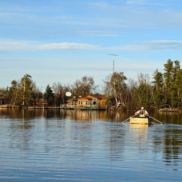 A person in a row boat on Brereton Lake with the Inverness Falls Resort office in the background