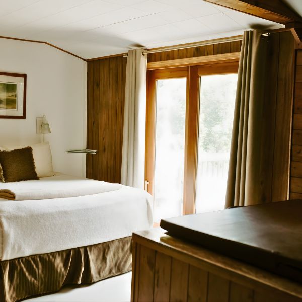 The bedroom area inside Cabin 6 at Inverness Falls Resort. It features a queen-sized bed, large windows, and an indoor hot tub.